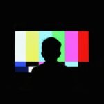 silhouette of boy in front of television screen with color bars