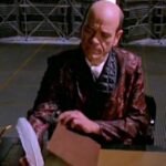 the doctor sitting a desk in a smoking jacket and writing with a quill pen from star trek voyager